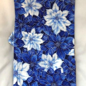 May include: A rectangular fabric item featuring a dense, repeating floral pattern of poinsettia-like flowers in shades of deep navy blue, royal blue, and bright white. The textile has visible stitched edges and a flat, folded construction.