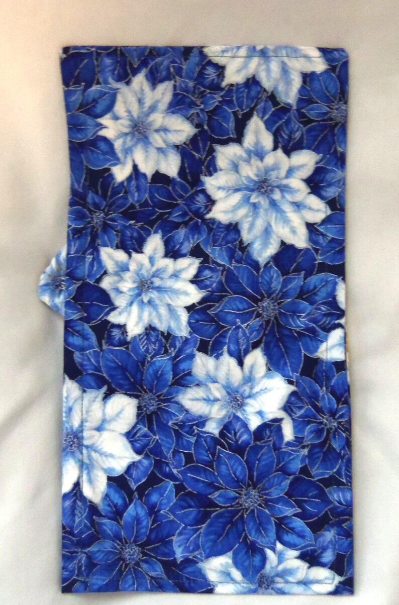 May include: A rectangular fabric item featuring a dense, repeating floral pattern of poinsettia-like flowers in shades of deep navy blue, royal blue, and bright white. The textile has visible stitched edges and a flat, folded construction.