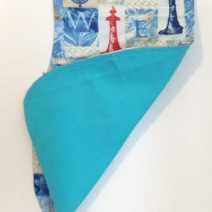 May include: A nautical-themed fabric item with a blue and white pattern featuring compasses, lighthouses, and rope designs. The item has a bright turquoise blue interior. The fabric is folded over, revealing the contrasting interior color.