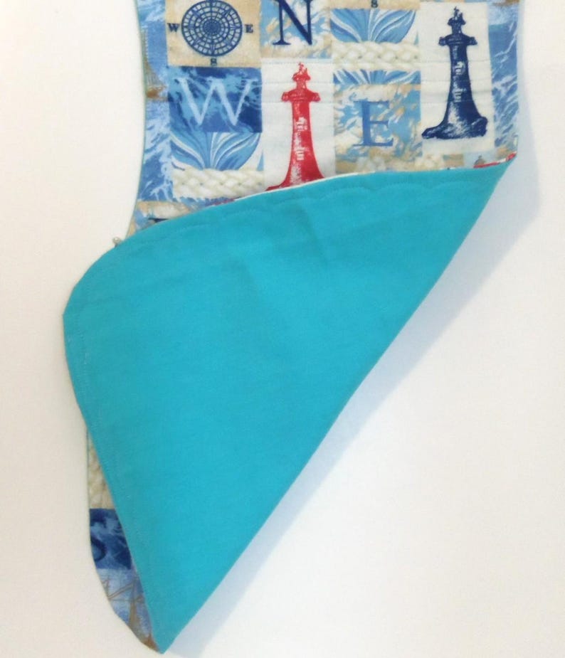 May include: A nautical-themed fabric item with a blue and white pattern featuring compasses, lighthouses, and rope designs. The item has a bright turquoise blue interior. The fabric is folded over, revealing the contrasting interior color.