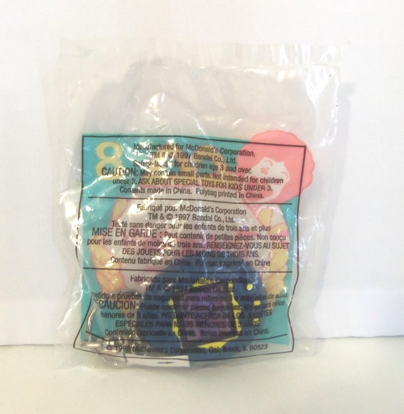 Puede incluir: Una bolsa de pl&aacute;stico transparente sellada que contiene un juguete promocional de McDonald's de 1997 de Bandai. El empaque presenta texto impreso en ingl&eacute;s, franc&eacute;s y espa&ntilde;ol, incluyendo advertencias de seguridad e informaci&oacute;n de fabricaci&oacute;n.