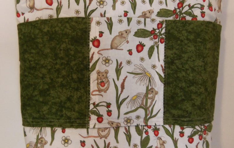 May include: A fabric item featuring a central panel of white cloth with a repeating pattern of brown mice, red strawberries, and white flowers, flanked by two solid dark green textured fabric panels with visible horizontal stitching.