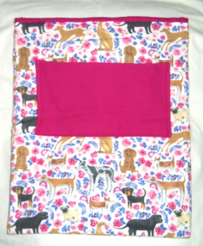 May include: A white fleece blanket with a pink fleece lining. The blanket features a repeating pattern of dogs and flowers.