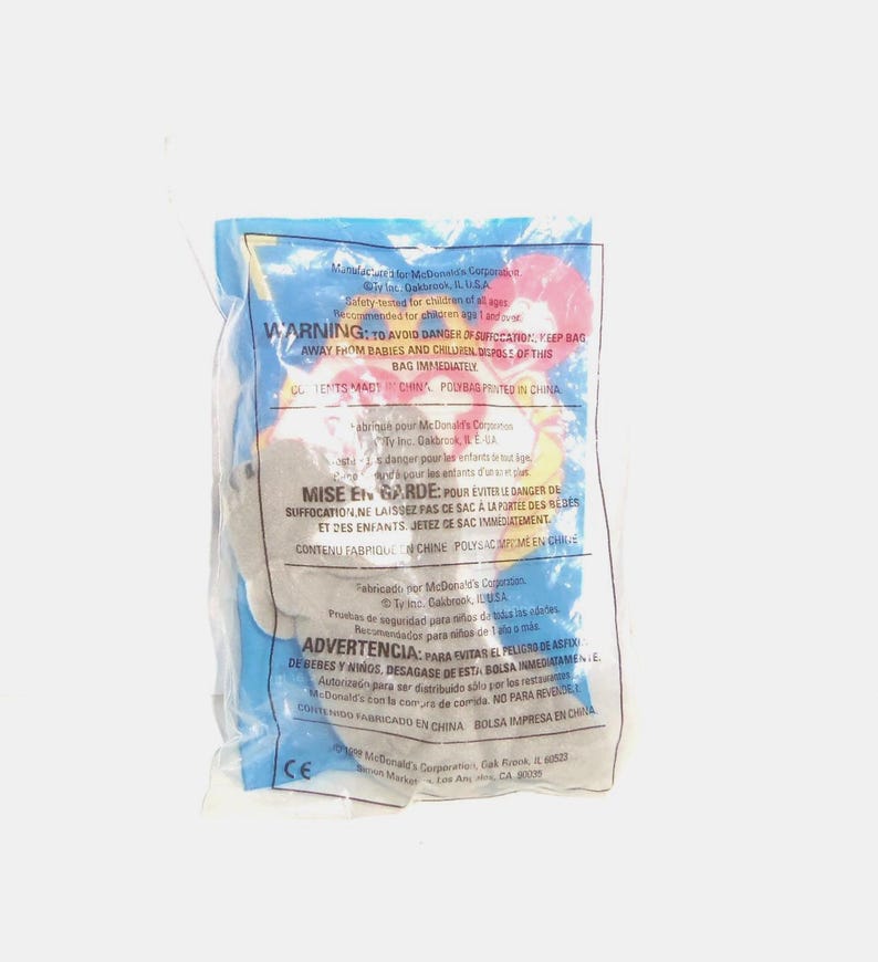 May include: A small, grey plush toy sealed inside a clear plastic bag. The packaging features printed safety warnings in English, French, and Spanish, along with the McDonald's Corporation logo and copyright information from 1999, all in black text.