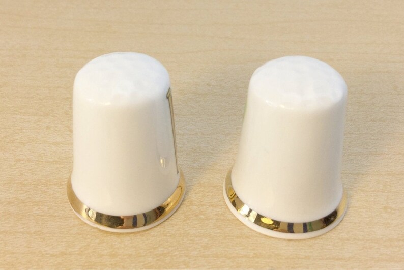May include: Two white ceramic thimbles with a gold trim around the top edge.