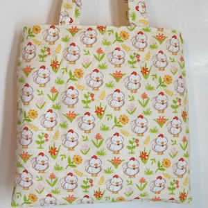 May include: A quilted tote bag made of cream-colored fabric featuring a repeating pattern of white chickens with red combs, yellow sunflowers, and green grass stalks. The bag includes two matching fabric handles at the top for carrying.