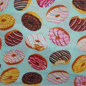 May include: A light blue fabric featuring a repeating pattern of various donuts with different colored glazes, including chocolate, pink, yellow, and white, decorated with colorful sprinkles and icing drizzles throughout the entire surface.