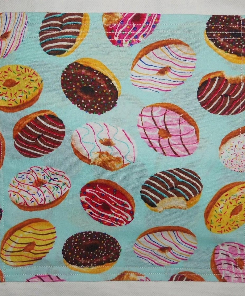 May include: A light blue fabric featuring a repeating pattern of various donuts with different colored glazes, including chocolate, pink, yellow, and white, decorated with colorful sprinkles and icing drizzles throughout the entire surface.