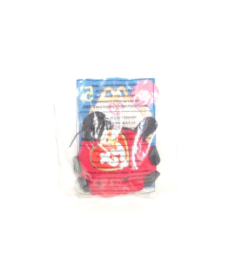 May include: A red and black plush toy sealed in a clear plastic bag. The packaging features the Ty logo and printed text including Manufactured for McDonald's Corporation, 2000 Ty Inc., and recommended for children age 1 and over.