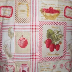 May include: A quilted fabric featuring a grid pattern with red and white gingham borders. The design includes illustrations of strawberries, a bowl of berries, a sugar jar, and a spoon, alongside printed text about strawberry jam recipes.