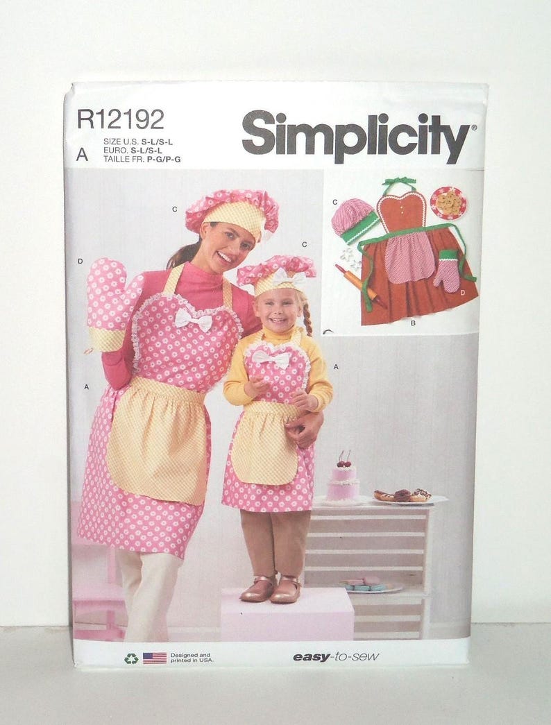 May include: Simplicity sewing pattern featuring a mother and child wearing matching pink polka dot aprons, oven mitts, and chef hats. The pattern includes a diagram of the apron design and the words "easy-to-sew".