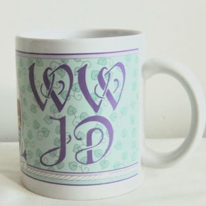 May include: A white ceramic mug featuring a light green background with a repeating pattern of small leaves. The center displays the purple stylized letters WD and JD in a decorative script font, framed by thin purple lines and a rope-like border.
