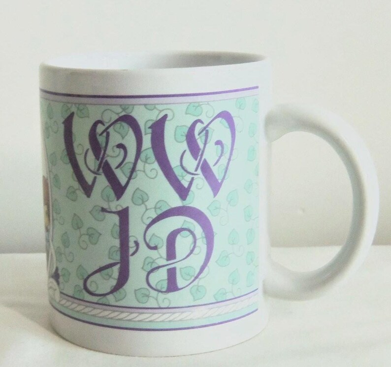May include: A white ceramic mug featuring a light green background with a repeating pattern of small leaves. The center displays the purple stylized letters WD and JD in a decorative script font, framed by thin purple lines and a rope-like border.