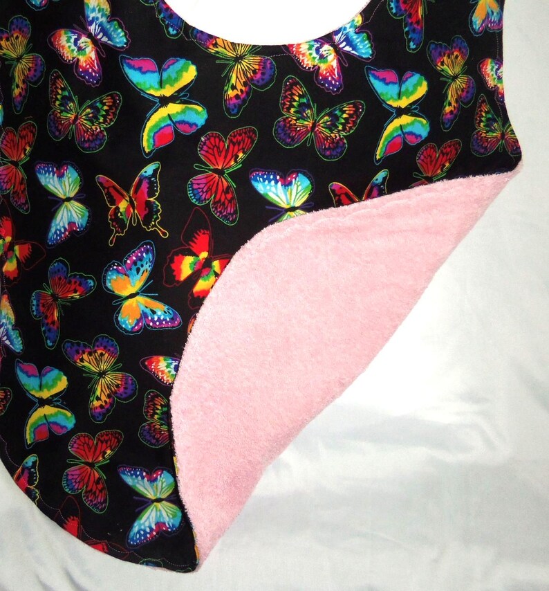 May include: A black bib with a colorful butterfly pattern on one side and a pink terry cloth backing on the other side.
