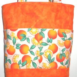 May include: Orange tote bag with a vibrant orange fabric and a band of white fabric featuring orange fruit illustrations. The handles are made of the same orange fruit pattern fabric. The bag is designed for carrying items.