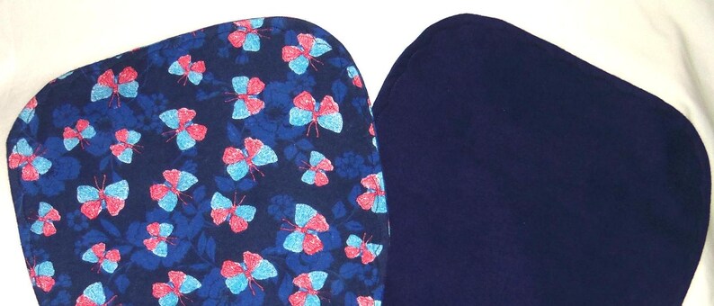 May include: Two fabric squares, one with a blue background and a pattern of pink and blue butterflies, and the other a solid dark blue.