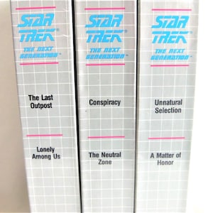 May include: Three Star Trek: The Next Generation VHS tapes with silver spines featuring a white grid pattern and bright blue text. The titles include The Last Outpost, Lonely Among Us, Conspiracy, The Neutral Zone, Unnatural Selection, and A Matter of Honor.