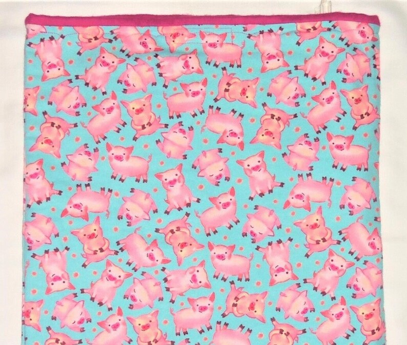 May include: A rectangular, light blue fabric with a repeating pattern of pink cartoon pigs in various poses. The fabric has a pink border. The pigs are in different positions, some upside down, with small orange dots scattered throughout.