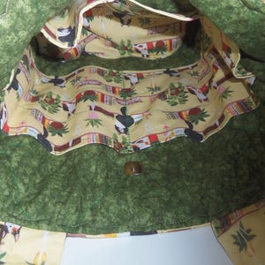May include: A quilted tote bag with a dark green exterior and a light yellow interior lining featuring a repeating pattern of cats, potted plants, and books. The bag includes a magnetic snap closure and multiple interior pockets for organization.