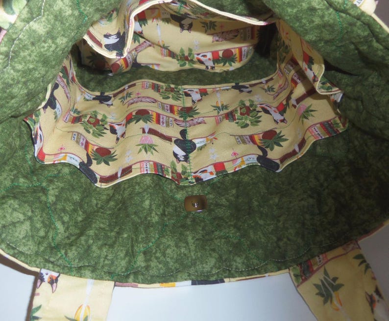 May include: A quilted tote bag with a dark green exterior and a light yellow interior lining featuring a repeating pattern of cats, potted plants, and books. The bag includes a magnetic snap closure and multiple interior pockets for organization.