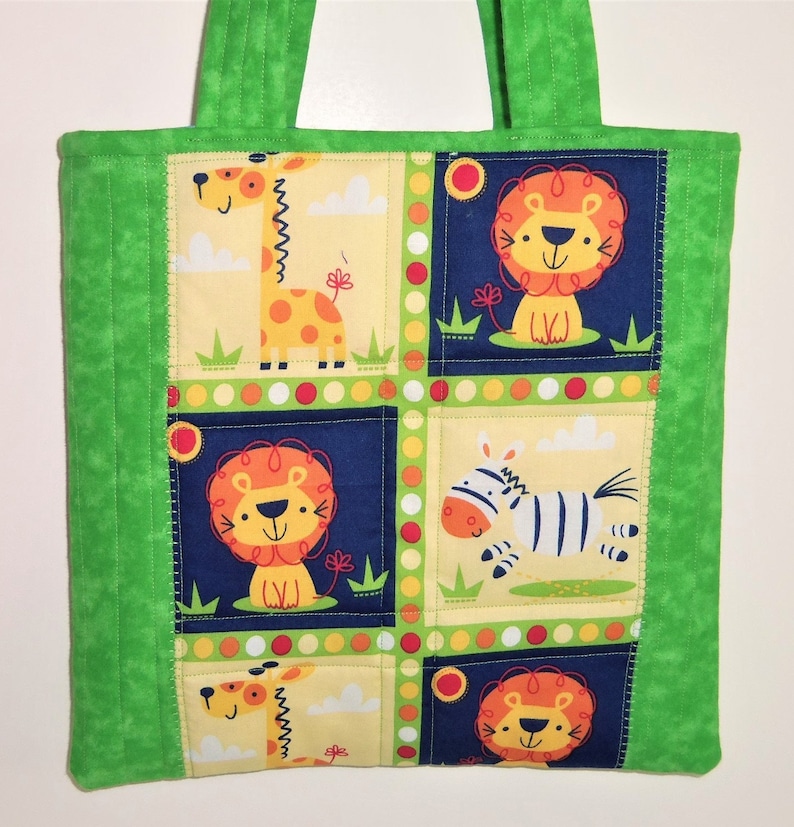 May include: A quilted tote bag featuring a vibrant green border and handles. The central panel displays a grid pattern with cartoon illustrations of giraffes, lions, and a zebra against yellow and dark blue backgrounds with colorful polka dots.