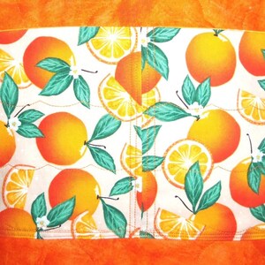 May include: A fabric with a vibrant orange and white pattern featuring oranges, orange slices, green leaves, and white blossoms. The fabric is bordered by solid orange fabric.