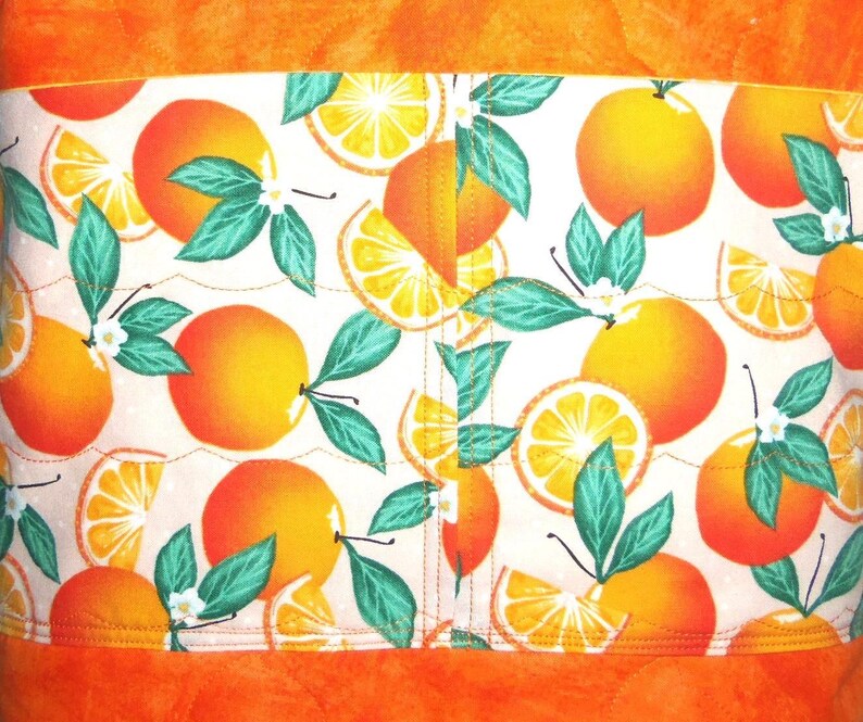 May include: A fabric with a vibrant orange and white pattern featuring oranges, orange slices, green leaves, and white blossoms. The fabric is bordered by solid orange fabric.