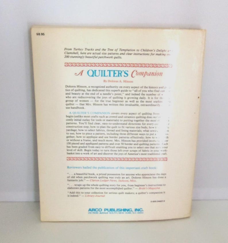 Puede incluir: La contraportada de un libro de tapa blanda titulado A Quilter's Companion de Dolores A. Hinson. La cubierta de color blanco hueso presenta texto impreso en negro que describe el contenido, incluyendo instrucciones para 200 colchas.