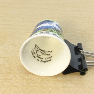 May include: White ceramic thimble with a blue and green floral design. The bottom of the thimble reads "Finsbury China Fine Bone China Made in England".