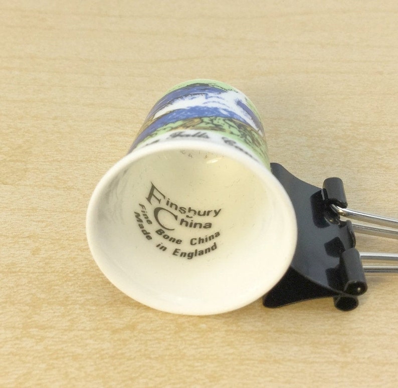 May include: White ceramic thimble with a blue and green floral design. The bottom of the thimble reads "Finsbury China Fine Bone China Made in England".