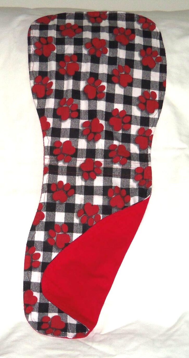 May include: A red and white checkered fabric dog bandana with red paw prints. The bandana has a red fleece lining.