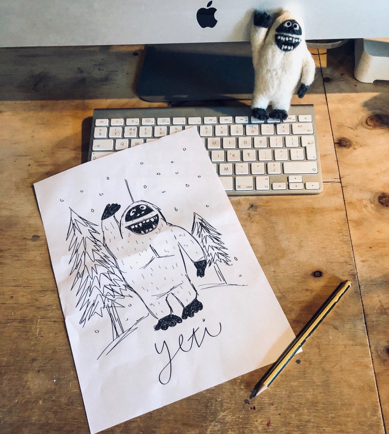 May include: A black and white drawing of a yeti waving with a snowy background and the word "yeti" written below. A small white yeti plush toy is sitting on a computer keyboard in the background.