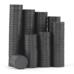 May include: A collection of small, round, black magnets arranged in several stacks of varying heights. One magnet rests on its side in front of the stacks. The magnets are uniformly sized and have a matte finish, set against a white background.