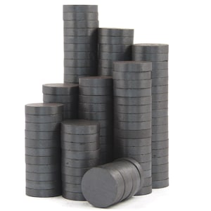 May include: A collection of dark gray, round magnets arranged in various stacks. The magnets are uniformly sized and stacked neatly, creating a visually appealing display. The image is set against a plain white background.