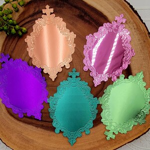 May include: Five die-cut paper shapes in a shield-like frame design with ornate, embossed scrollwork borders. The colors include metallic copper, reflective magenta, deep purple, teal, and light green, all featuring a smooth, glossy finish.