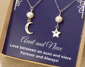 May include: A gift box containing two necklaces with pearl charms. One necklace features a crescent moon charm with the letter "S" and the other necklace features a star charm with the letter "P". The box has a blue background with the text "Aunt and Niece Love between an aunt and niece Forever and Always!"