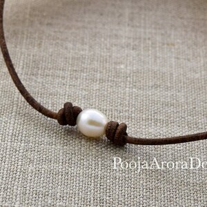 May include: A simple brown leather cord necklace with a single white pearl tied in a knot.