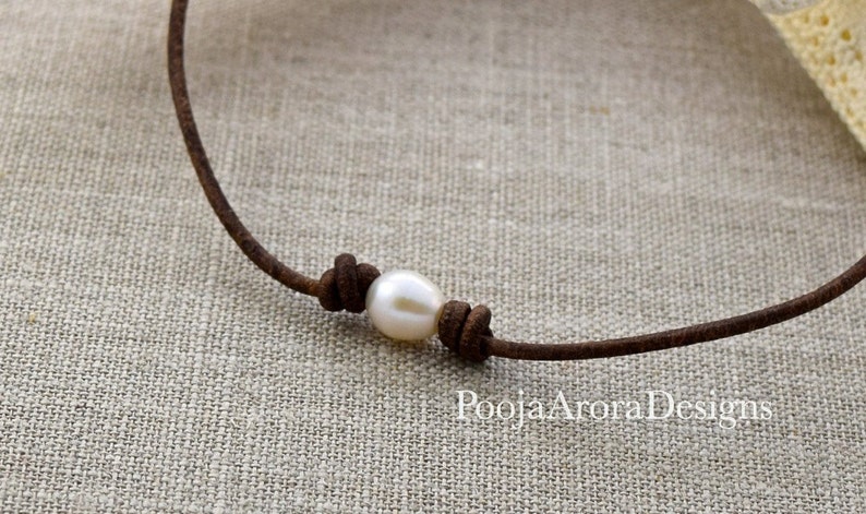 May include: A simple brown leather cord necklace with a single white pearl tied in a knot.