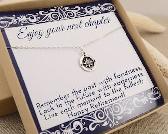 May include: A silver compass pendant necklace displayed in a gift box. The box contains a card with the text "Enjoy your next chapter" and "Happy Retirement!" The necklace is on a white card with a navy blue border.