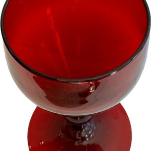 May include: A red glass goblet with a wide bowl and a short stem. The goblet has a round base.