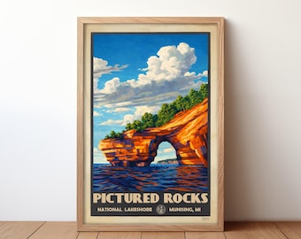 May include: Framed art print featuring a scenic view of Pictured Rocks National Lakeshore in Munising, MI. The artwork depicts a natural rock formation with an archway, lush green trees, and a blue sky with fluffy white clouds. The print is in a light wood frame.