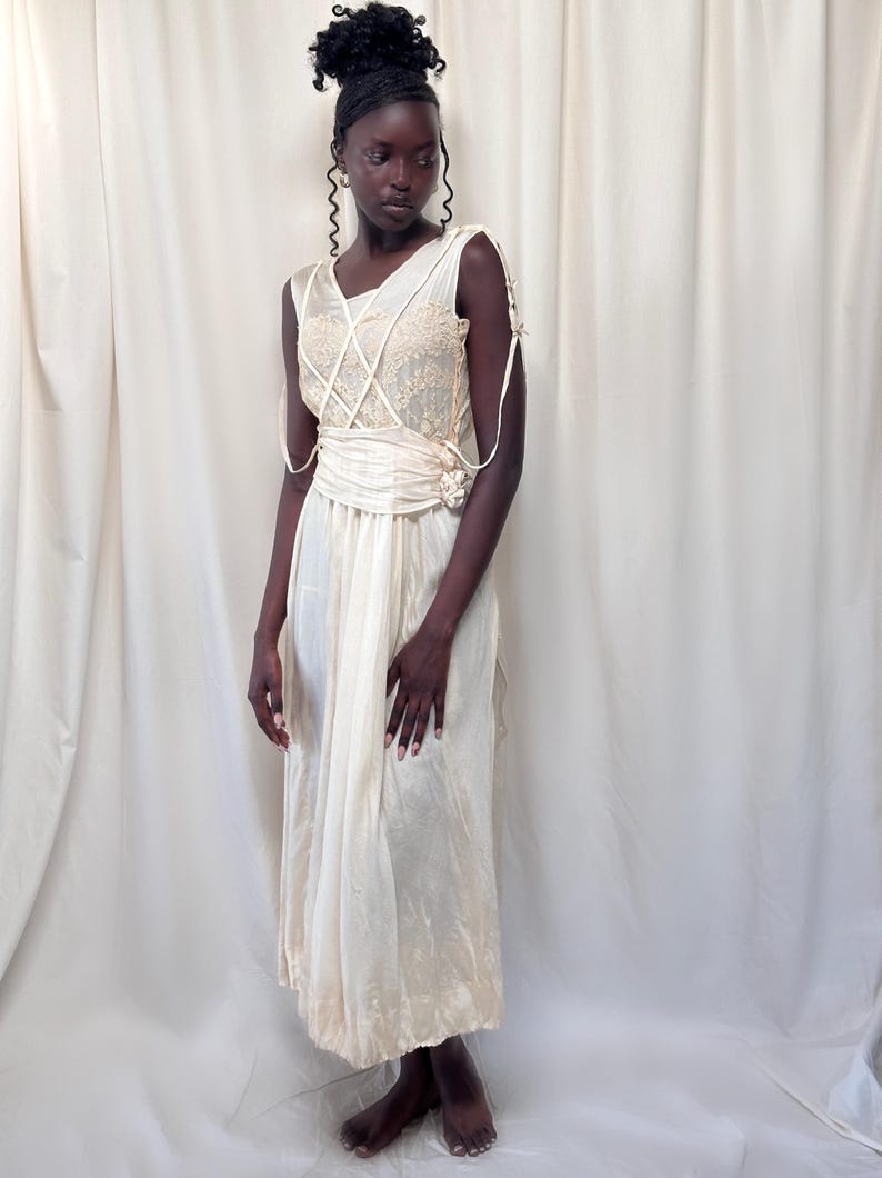May include: A white sleeveless dress with a lace bodice and a sash. The dress has a flowing skirt and is made of a lightweight fabric.
