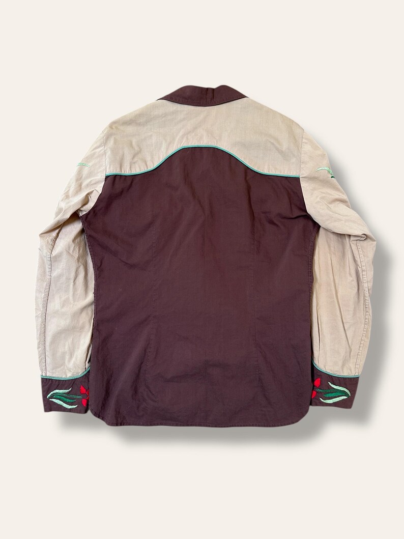 May include: Back view of a western-style shirt. The shirt features a brown body with tan sleeves and yoke. The design includes turquoise trim and red floral embroidery on the cuffs.