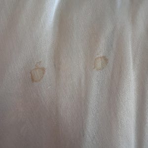 May include: Two light brown stains on a white fabric surface.