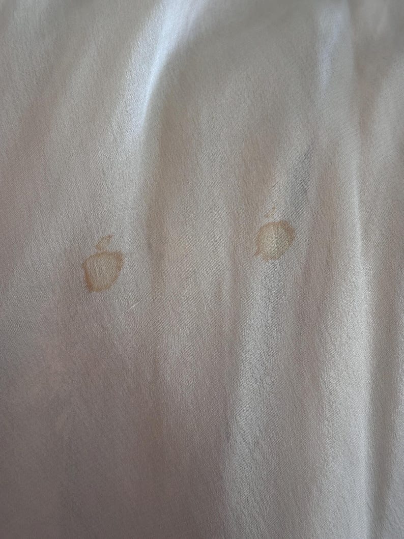May include: Two light brown stains on a white fabric surface.