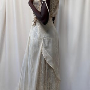May include: A white vintage dress with a lace overlay and a satin bodice. The dress has a fitted bodice and a flowing skirt.