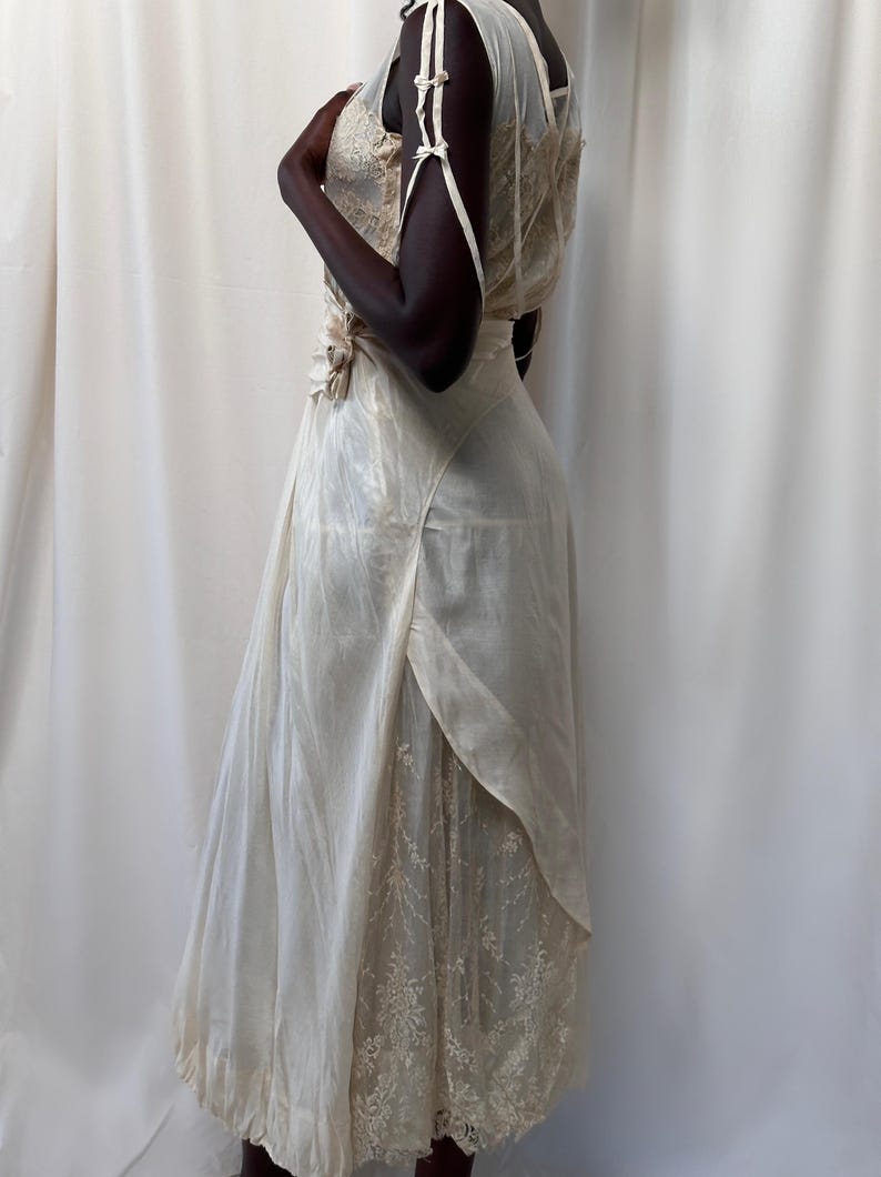May include: A white vintage dress with a lace overlay and a satin bodice. The dress has a fitted bodice and a flowing skirt.