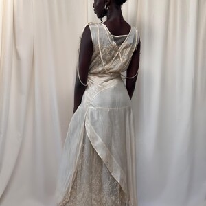 May include: A white vintage dress with a lace overlay and a satin sash. The dress has a sleeveless design and a flowing skirt.