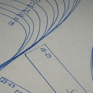 Op de afbeelding: Een close-up van een wit oppervlak met blauwe lijnen en nummers. De nummers zijn met de hand geschreven en omvatten 18, 19, 20, 21, 22, 23, 27-29 en 16-29.