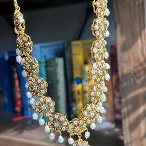 May include: A gold necklace with a floral design and white pearl accents. The necklace is made of metal and has a delicate, intricate design.